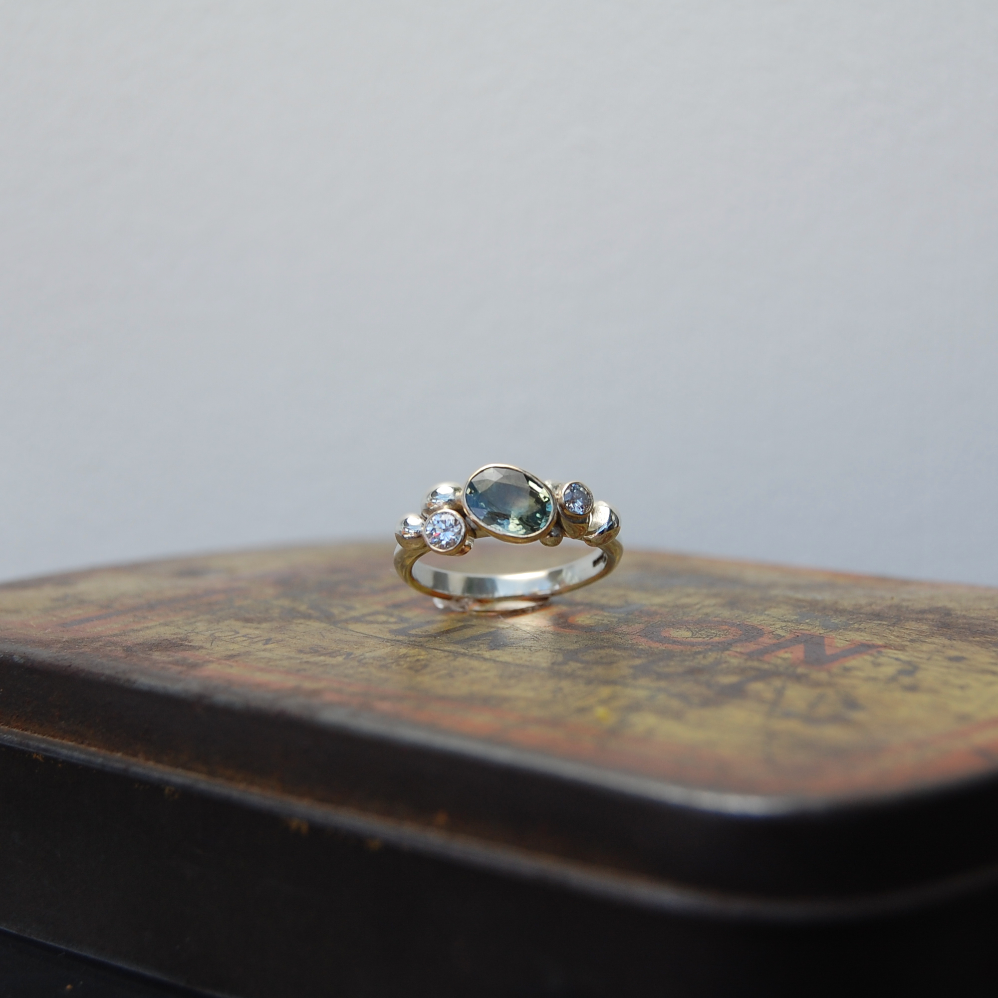 Pale green sapphire set in yellow gold cup setting with diamonds and white gold clusters on white gold ring