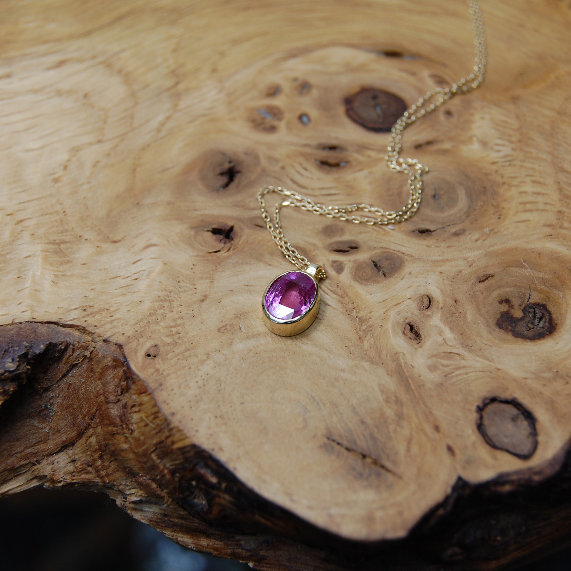 Oval pink sapphire set in 18ct yellow gold rub-over setting on 18inch curb chain