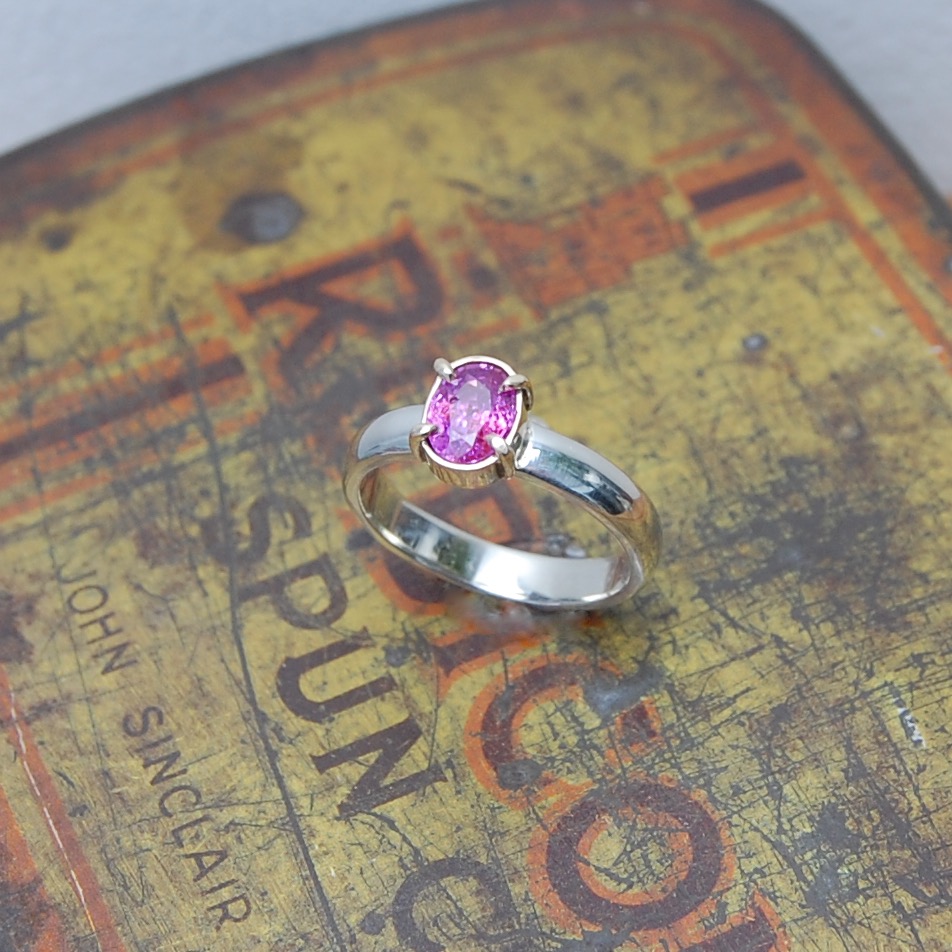 Oval pink sapphire set in 9ct yellow gold claw setting on a white gold band