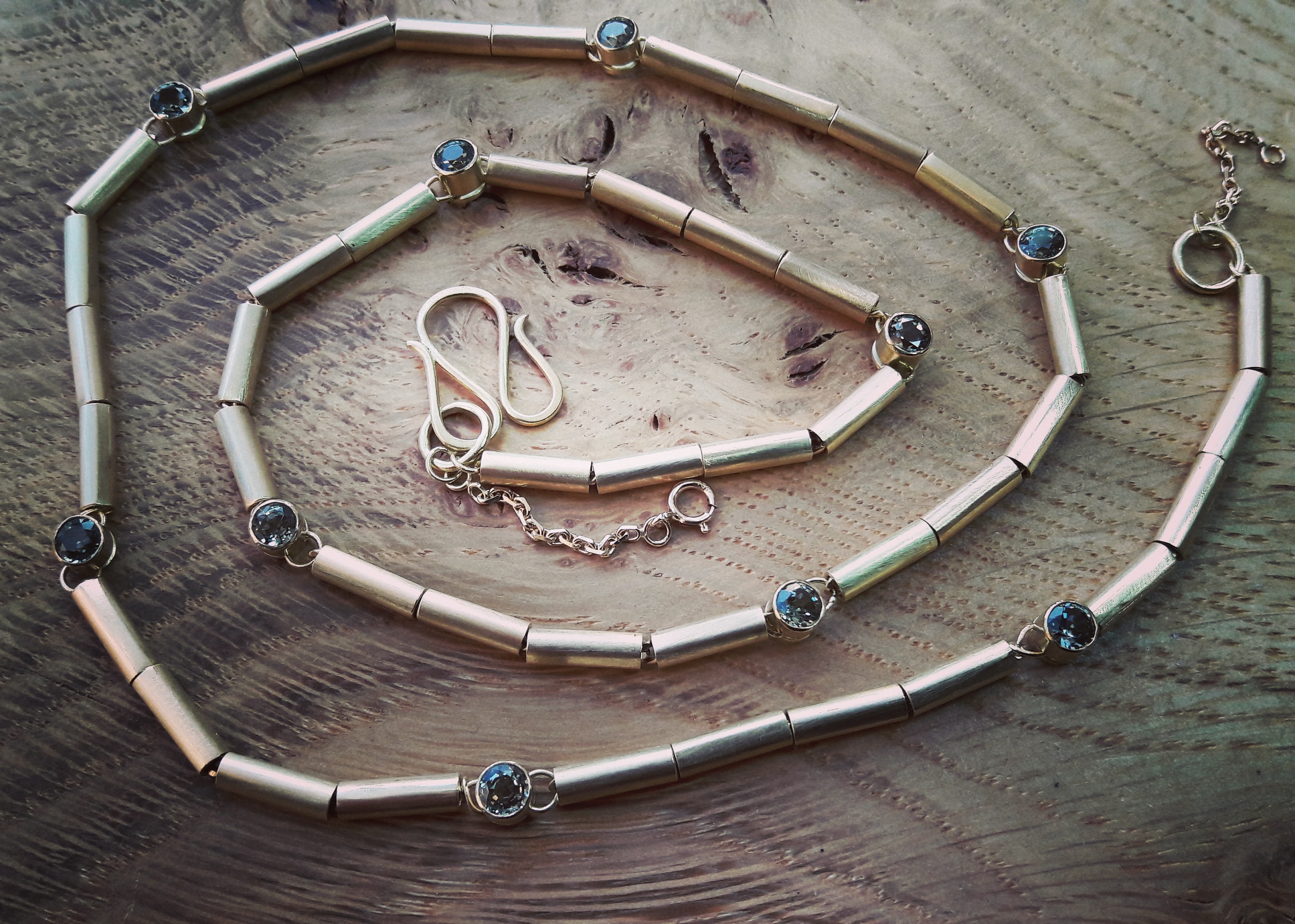 Gold tubes strung onto gold chain connected by tube set green sapphires